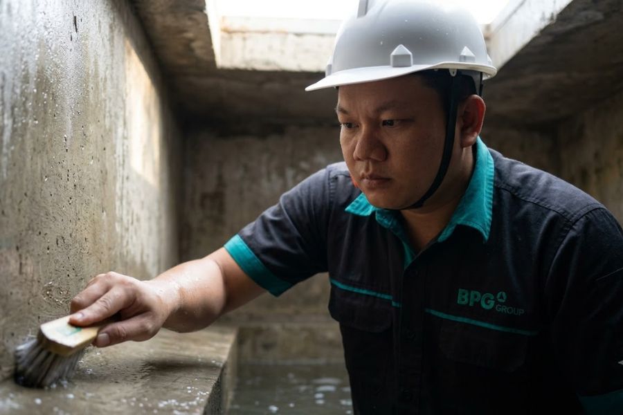 Nhân viên BPG đội mũ bảo hộ dùng bàn chải cọ góc thành bể nước ngầm