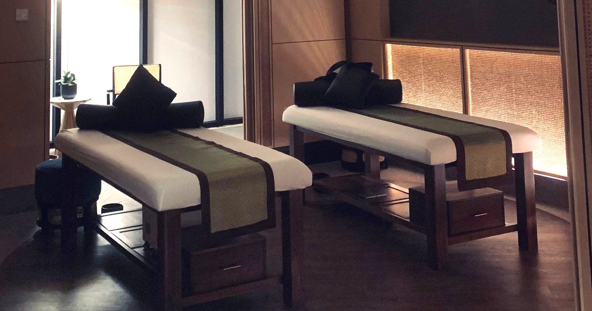 Phòng trị liệu spa có hai giường massage gỗ và đèn trần lớn